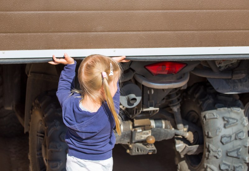 Child lifting a garage door, illustrating important garage door safety features in Chicago, IL